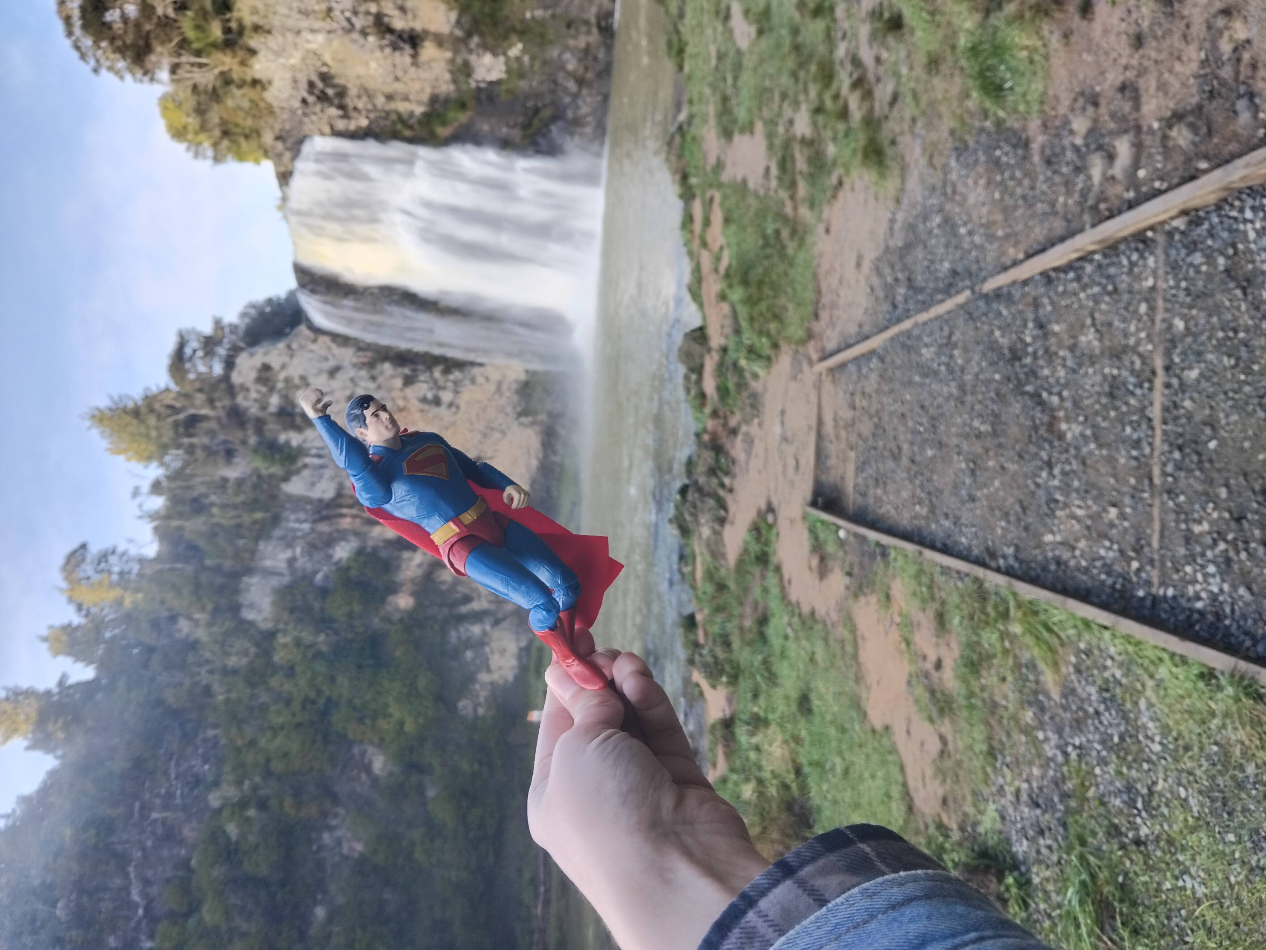 superman toy being held infront of a waterfall